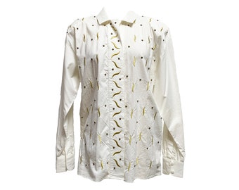 Puede incluir: Camisa blanca abotonada con mangas largas. La camisa tiene cuello y está adornada con pequeños puntos oscuros y diseños bordados curvos de color amarillo verdoso. La camisa está hecha de una tela ligera.