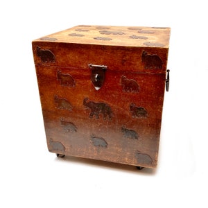 Könnte beinhalten: Eine Holzkiste mit brauner Oberfläche und einem Elefantenmuster. Die Kiste hat einen Metallverschluss und zwei Metallgriffe an der Seite.