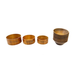 May include: Wooden serving bowls with the words "PRETZELS", "POTATO CHIPS", and "PEANUTS" printed on them. A stack of similar bowls is also present. The bowls are a light brown color and appear to be made of wood.