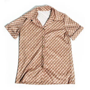 May include: A short-sleeved button-down shirt featuring a tan and brown diagonal plaid pattern. The garment has a wide collar, a front button placket with five visible buttons, and a white interior lining visible at the neckline area.