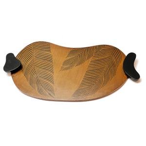 Op de afbeelding: Een houten dienblad met zwarte handvatten en een bladontwerp. Het dienblad is bruin en heeft een licht gebogen vorm.