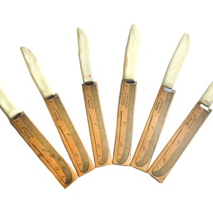 Juego vintage de 6 cuchillos para carne Quikut de acero inoxidable con mangos de tenite jaspeado de color blanco roto, incluye fundas de cartón originales.