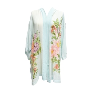 Op de afbeelding: Een lichtblauwe kimono-achtige robe met een bloemenontwerp. De robe heeft een lichtblauwe bies en is versierd met roze, paarse en oranje bloemen met groene bladeren. De robe is gemaakt van een lichtgewicht stof.