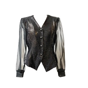 Puede incluir: Una blusa negra de lentejuelas con mangas largas transparentes y escote en V. La blusa tiene un cierre de botones en la parte delantera y una silueta ajustada.