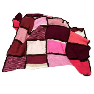 May include: A patchwork crocheted throw blanket in shades of pink, red, and brown. The blanket is made of squares of different colors and textures, and is arranged in a random pattern.