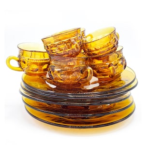 Könnte beinhalten: Ein Set aus Teetassen und Untertassen aus bernsteinfarbenem Glas. Die Tassen und Untertassen haben ein strukturiertes, erhabenes Design. Die Tassen sind übereinander gestapelt, und die Untertassen sind darunter gestapelt.