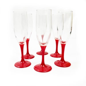 Puede incluir: Conjunto de seis copas de champán de vidrio transparente con tallos pintados de rojo. Las copas están dispuestas en semicírculo sobre un fondo blanco.