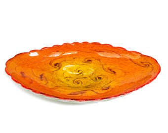 May include: A shallow, oval-shaped glass bowl featuring a vibrant gradient of yellow at the center transitioning into deep orange and red toward the scalloped edges. The surface displays a swirling, marbled pattern with dark, intricate wisps.