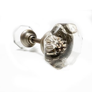 Puede incluir: Un pomo de puerta de vidrio transparente con un diseño facetado y una base de metal plateado.