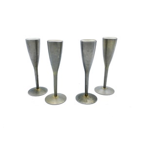 Puede incluir: Cuatro copas de champán vintage con un acabado plateado metálico. Cada copa tiene un tallo delgado y una base ancha y circular. Las copas están dispuestas sobre un fondo blanco.