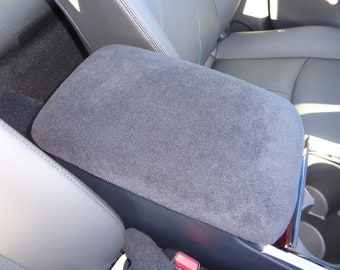 May include: A gray car armrest with a soft, plush fabric covering. The armrest has a built-in cup holder.