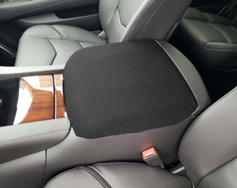 May include: Black car seat cover for a center console armrest. The cover is made of a soft, black fabric and has a smooth, flat surface.