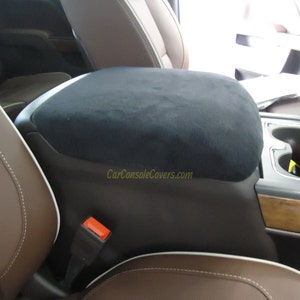 May include: Black suede center console armrest cover for a car. The cover is installed on a brown leather car seat with white stitching. The text "CarConsoleCovers.com" is visible on the cover.