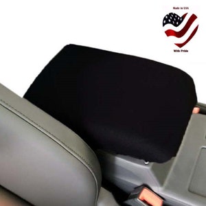 May include: Black car seat armrest cover. The cover is made of a soft, black fabric and is designed to protect the armrest from wear and tear.