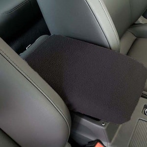 May include: Black car seat armrest cover with a soft, fuzzy texture. The cover is designed to protect the armrest from wear and tear.