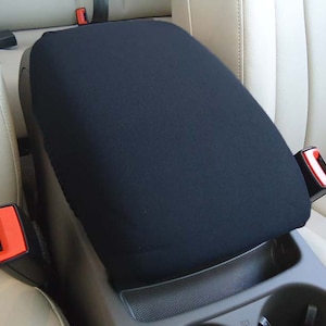 May include: Black car seat armrest cover. The cover is made of a soft, black fabric and fits snugly over the armrest. It is designed to protect the armrest from wear and tear.