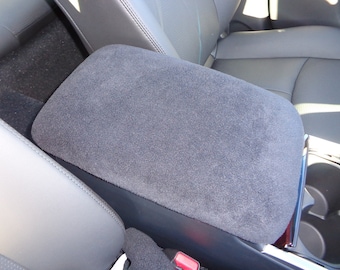 May include: A gray car seat armrest cover with a soft, plush texture. The cover is made of a thick, durable material and is designed to protect the armrest from wear and tear.