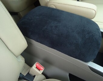 May include: Black suede armrest cover for a car. The cover is installed on a beige leather armrest.