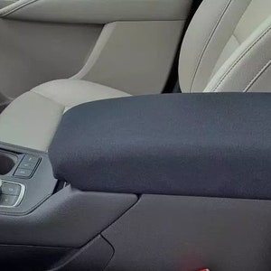 May include: A black car armrest cover with a gray fabric interior. The cover is made of a soft, durable material and is designed to protect the armrest from wear and tear.