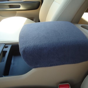 May include: A gray fleece car center console armrest cover. The cover is made of soft, plush fabric and is designed to protect the armrest from wear and tear.