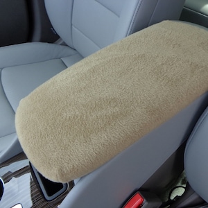 May include: Beige armrest cover for a car seat. The cover is made of a soft, plush fabric and is designed to protect the armrest from wear and tear.