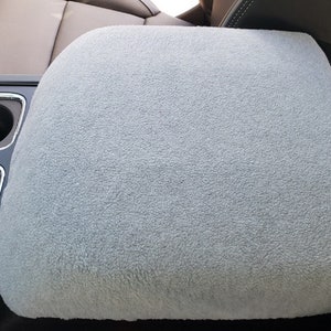 May include: Gray fleece car seat cover with a black border. The cover is designed to fit over the center console armrest of a car.