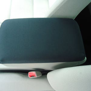 May include: Black fabric armrest cover for a car seat. The cover is made of a soft, durable material and is designed to protect the armrest from wear and tear.
