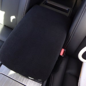 May include: Black fleece car armrest cover. The cover is installed on a black leather car seat.