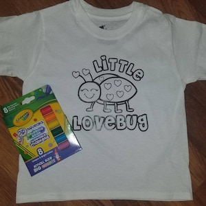 May include: White t-shirt with a black and white outline of a ladybug with the text "Little Lovebug". A pack of 8 Crayola Pip-Squeaks washable markers is included.