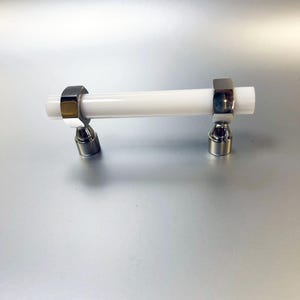 May include: White ceramic cabinet pull with chrome accents. The pull is cylindrical in shape with rounded ends.