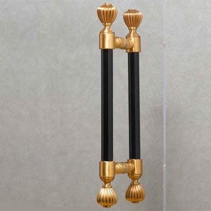 May include: A pair of black and gold door handles with ornate, decorative finials. The handles are attached to a glass door.