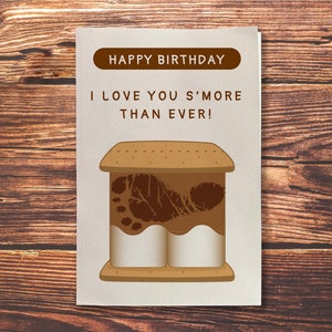 Puede incluir: Una tarjeta de cumpleaños con una ilustración de s'more y el texto "Feliz cumpleaños Te quiero más que nunca!"