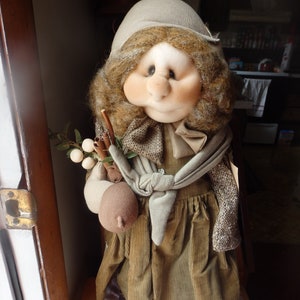 May include: A handmade doll with a brown corduroy dress, a white scarf, and brown hair. The doll is holding a bundle of cinnamon sticks and white berries.