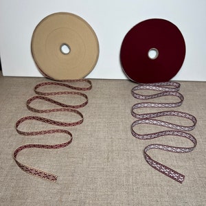 Può includere: Due bobine di passamaneria decorativa con un motivo geometrico. La passamaneria a sinistra è beige con un motivo bordeaux. La passamaneria a destra è bordeaux con un motivo bianco.