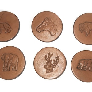 May include: Six brown leather coasters with embossed animal designs: a wolf, horse, bison, elephant, deer, and bear. The coasters are round and have a rustic, natural appearance, perfect for home decor.