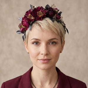 Könnte beinhalten: Eine Frau trägt einen bordeauxfarbenen Blazer und einen Blumenkranz. Der Kranz hat tiefrote und goldene Blumen mit dunklen Blättern. Eine zarte Halskette und goldene Ohrstecker vervollständigen den Look.