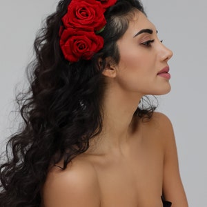 May include: A woman with long, curly black hair wearing a headband with red roses. She is wearing a black strapless top and has a natural makeup look.