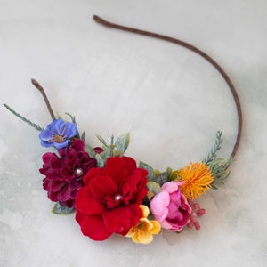 May include: A floral headband with a brown wire frame and colorful fabric flowers. The flowers are red, pink, yellow, blue, and orange.