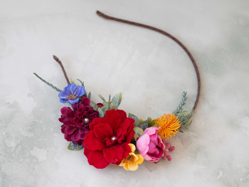 May include: A floral headband with a brown wire frame and colorful fabric flowers. The flowers are red, pink, yellow, blue, and orange.