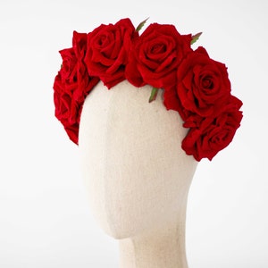 May include: A red rose flower crown with green leaves. The crown is on a white mannequin head.
