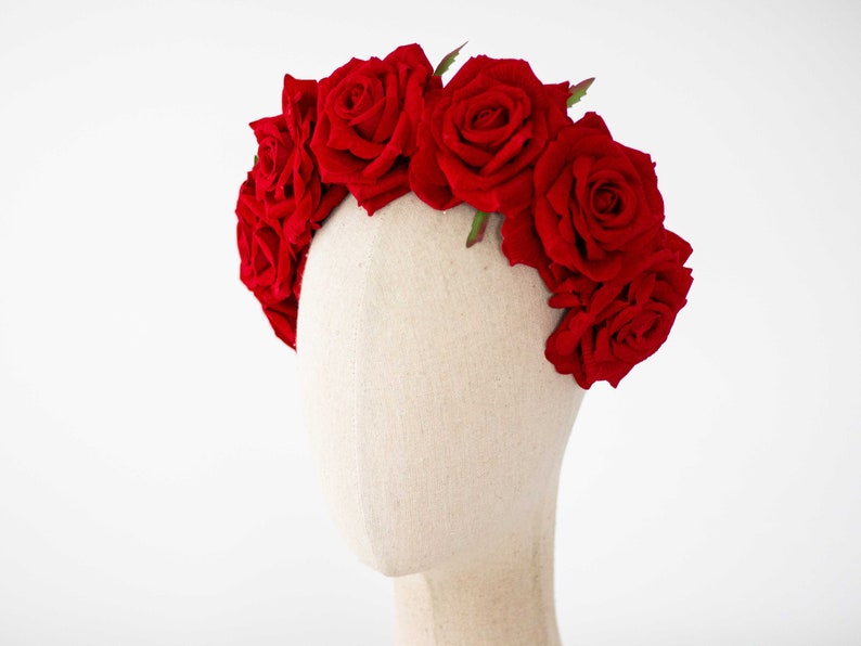May include: A red rose flower crown with green leaves. The crown is on a white mannequin head.