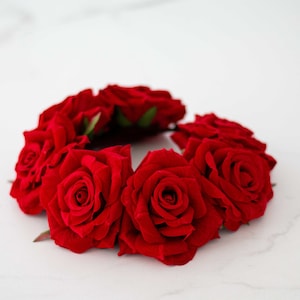 May include: A red rose hair wreath with six roses arranged in a circle. The roses are made of fabric and have a velvety texture.