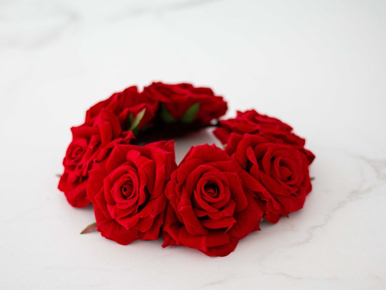 May include: A red rose hair wreath with six roses arranged in a circle. The roses are made of fabric and have a velvety texture.
