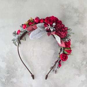 Könnte beinhalten: Ein floraler Haarreif mit tiefroten Rosen, Beeren und Blättern. Der Haarreif hat einen braunen Drahtrahmen und ist mit gefrorenen silbernen Blättern verziert. Dieses dekorative Kopfstück ist für besondere Anlässe geeignet.