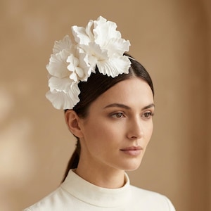 Peut inclure: Un coiffe floral blanc avec de grands pétales froissés. La coiffe est portée sur la tête et est faite d'un matériau léger. La femme sur l'image porte un haut blanc et a les cheveux foncés.
