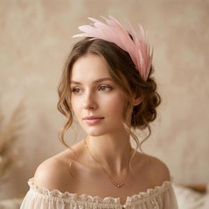 Peut inclure: Un accessoire de tête en plumes rose pâle composé d'une série de plumes superposées et dressées en forme d'éventail. Cet ornement capillaire présente une palette de couleurs monochrome douce et une structure délicate basée sur des plumes fines.