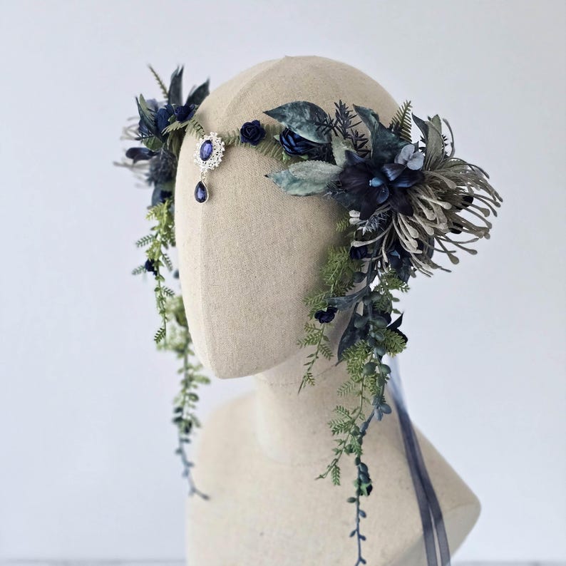 Pode incluir: Uma grinalda floral com flores e folhagens artificiais azuis escuros e verdes. Um detalhe central com joias e uma gema azul pendurada. Folhagens longas e fitas azuis completam o design. Ideal para ocasi&otilde;es especiais.