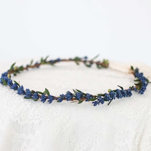 Puede incluir: Una corona de flores azul con pequeñas flores delicadas y hojas verdes. La corona está hecha de una base de alambre delgado y es perfecta para una boda u otra ocasión especial.