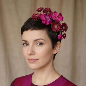 Könnte beinhalten: Eine Frau mit kurzen, dunklen Haaren, die einen floralen Haarschmuck trägt. Der Haarschmuck besteht aus tiefrosa und magenta farbenen Blumen. Sie trägt ein magenta- und bordeauxfarbenes Oberteil.