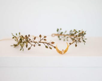 May include: A gold crescent moon charm with a single clear crystal in the center, attached to a delicate wire vine with small green leaves and clear crystal accents.
